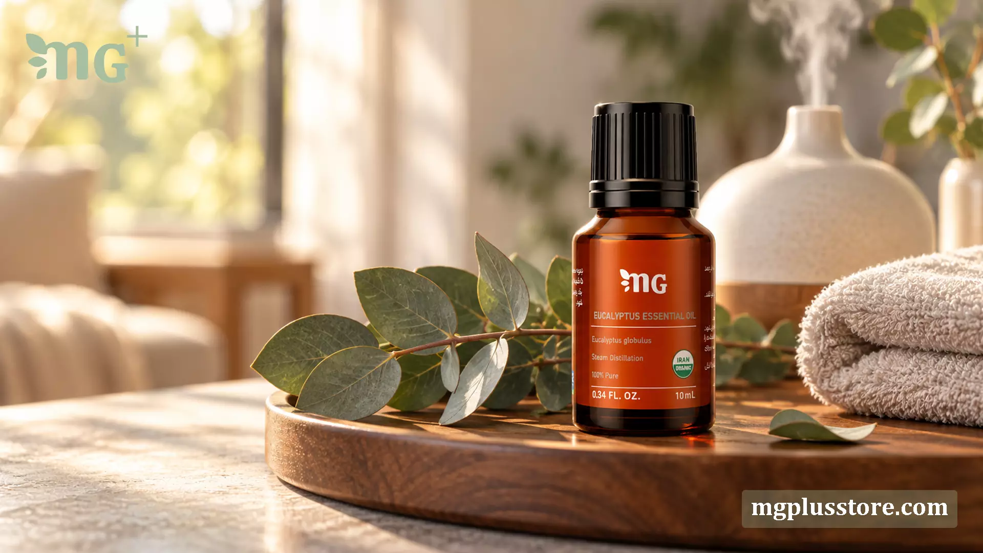 شیشه ۱۰ میلی‌لیتری اسانس گیاهی اکالیپتوس ام جی پلاس (MG Plus) با خلوص ۱۰۰ درصد و نشان ارگانیک ایران، قرار گرفته روی پایه چوبی در کنار برگ‌های تازه اکالیپتوس، حوله و دستگاه بخور (دیفیوزر) برای رایحه‌درمانی.